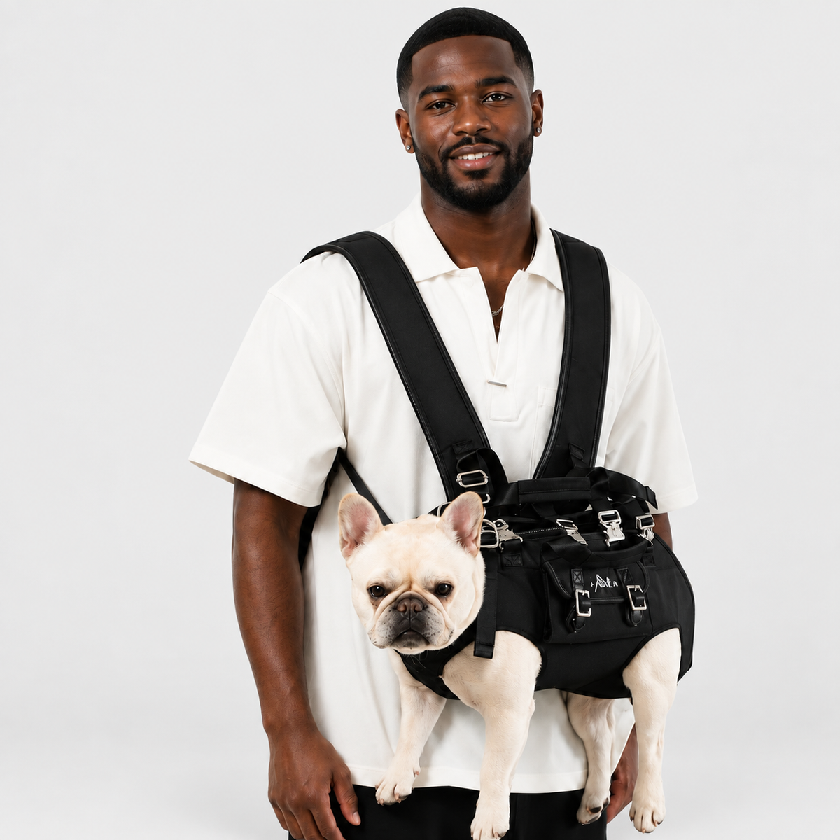 Man carrying a French Bulldog in a black dog carrier on a light gray background