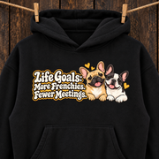 Woman wearing a black French Bulldog hoodie with the Life Goals: More Frenchies. Fewer Meetings front print.
