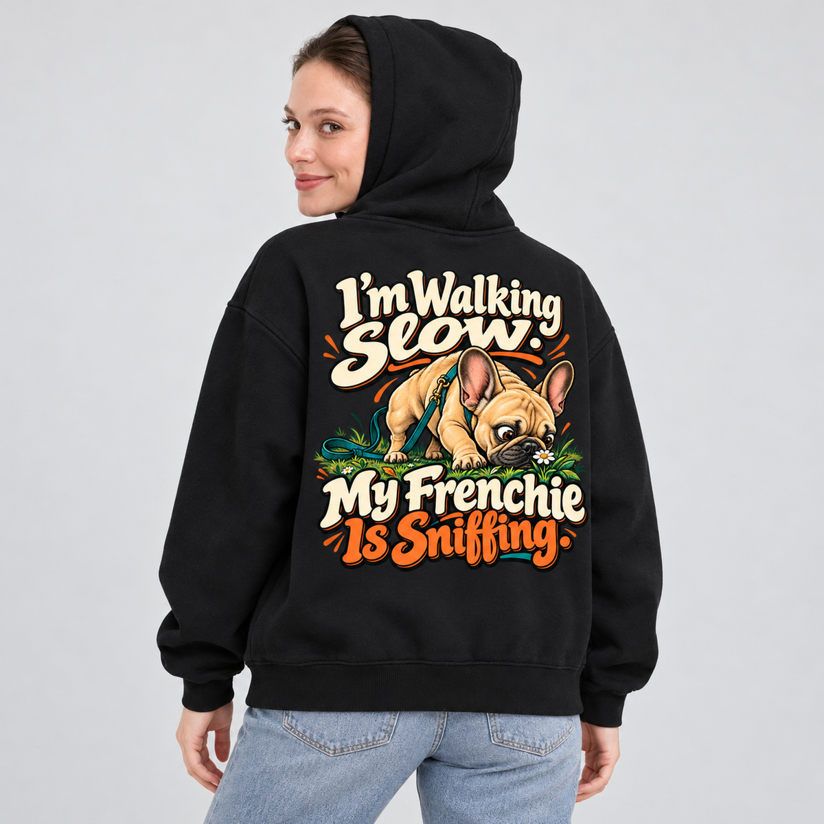 Woman wearing a black French Bulldog hoodie with the I'm Walking Slow. My Frenchie Is Sniffing back print.