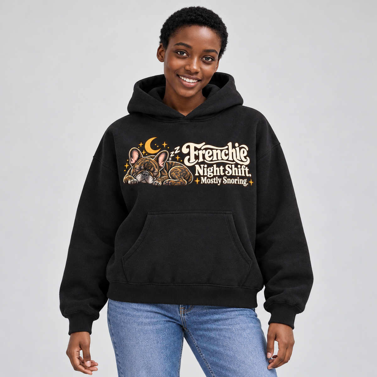 Woman wearing a black French Bulldog hoodie with the Frenchie Night Shift. Mostly Snoring front print.