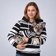 Woman looking at the camera wearing a matching black and white striped human hoodie and holding a French Bulldog