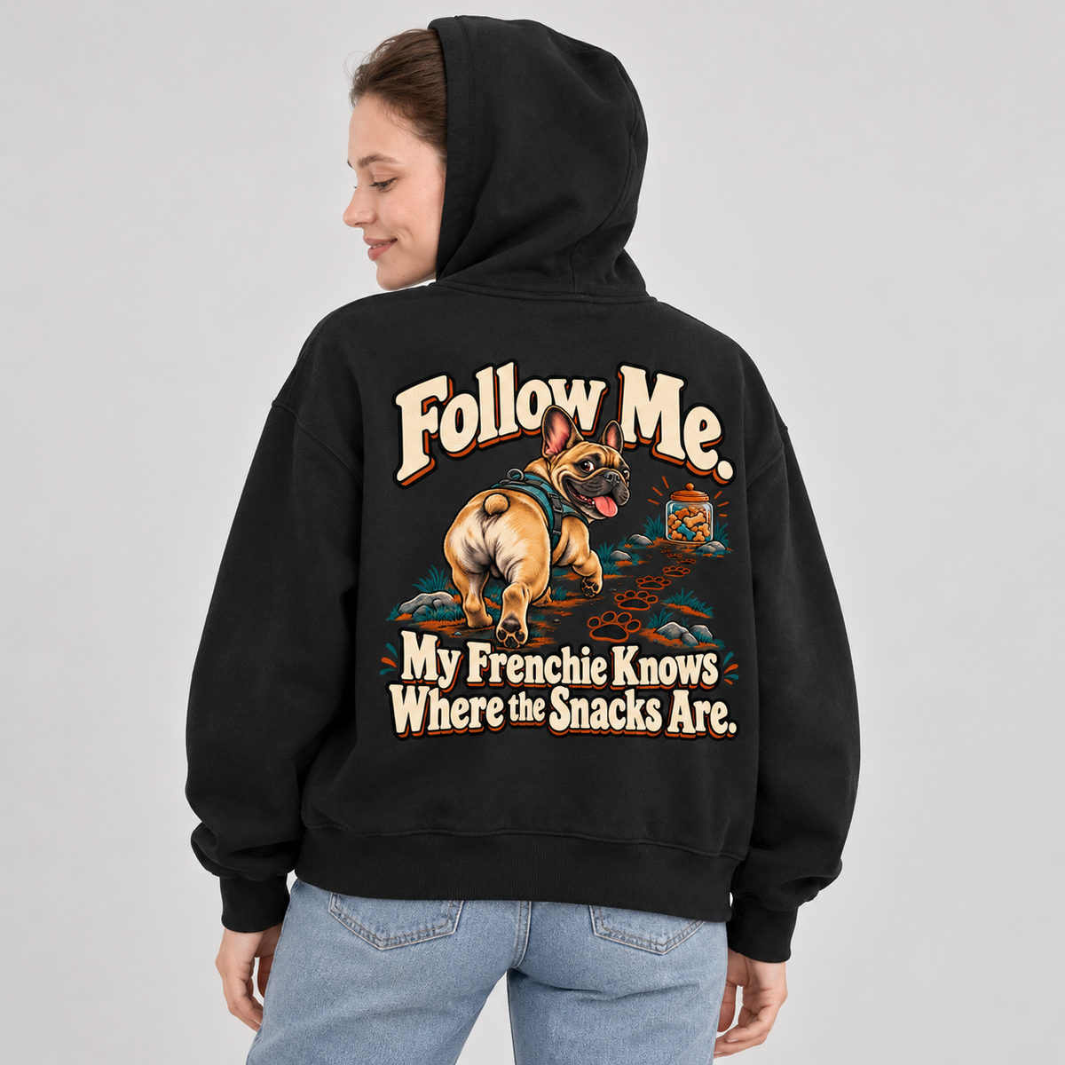 Woman wearing a black French Bulldog hoodie with the Follow Me. My Frenchie Knows Where the Snacks Are back print.